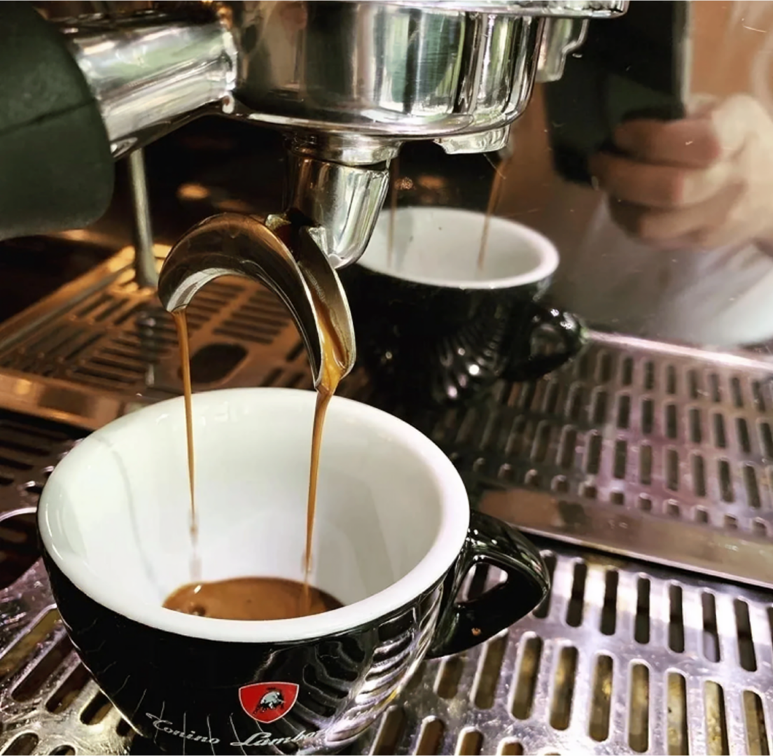 Espresso machine pouring coffee into a black cup on a metal drip tray.